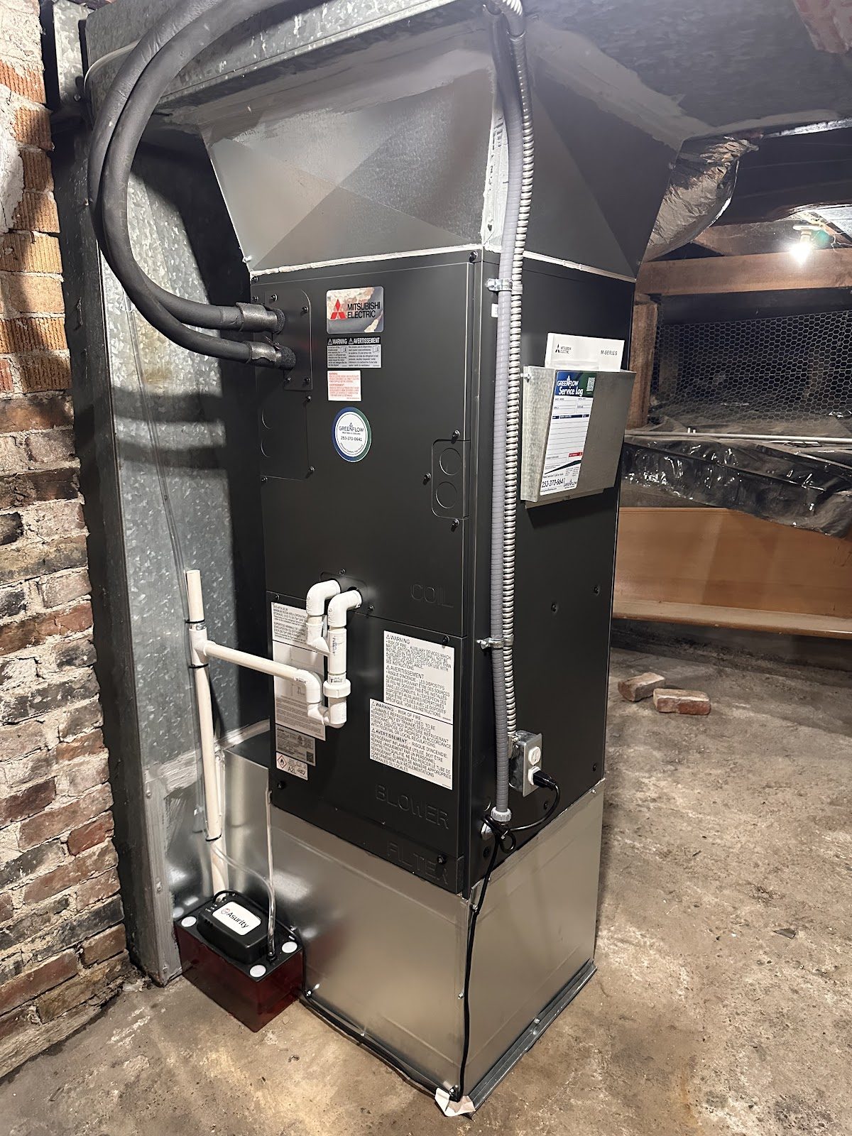 Vertical Mitsubishi gas furnace installed in a basement mechanical room with brick chimney