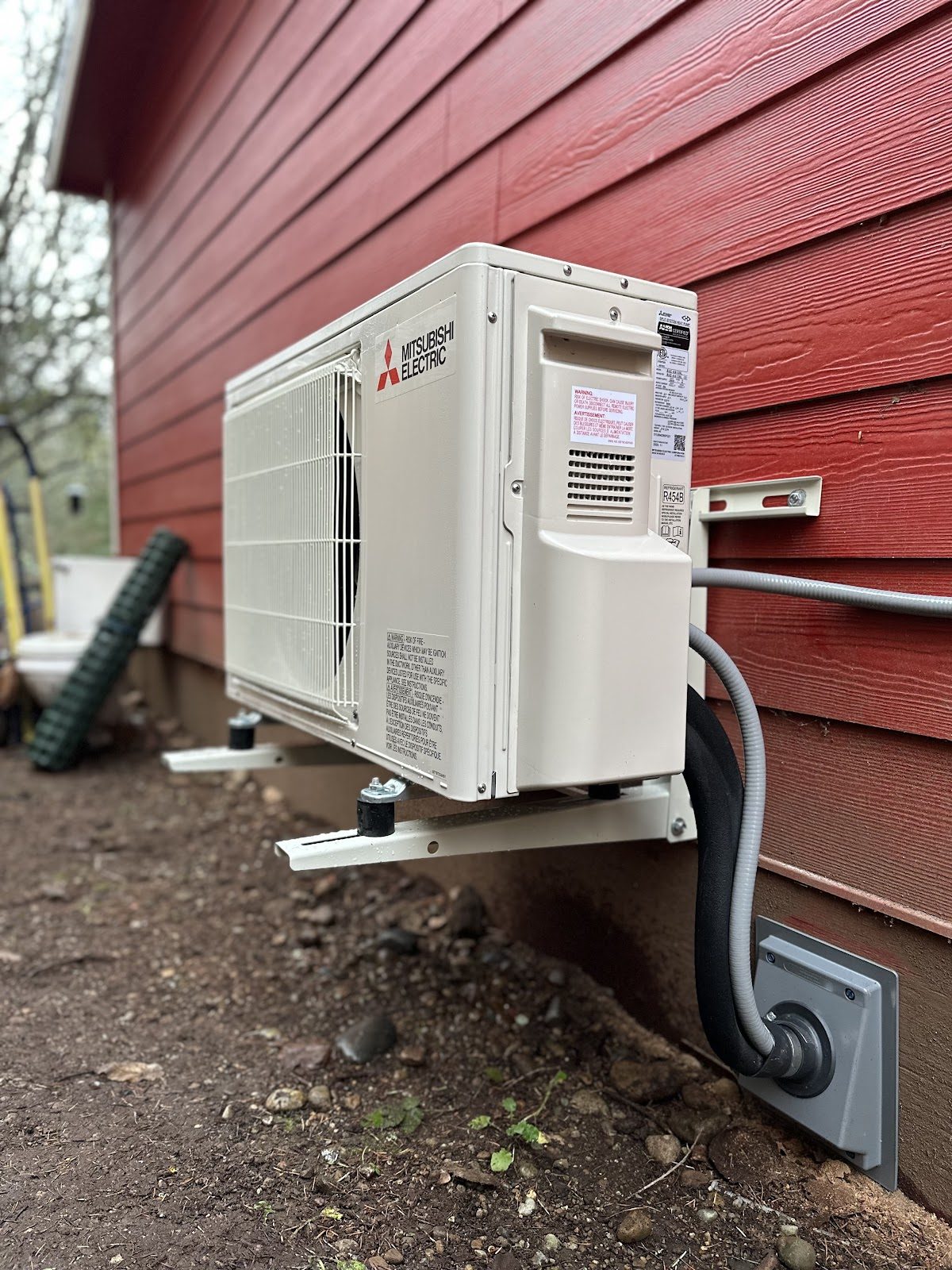 Mitsubishi ductless outdoor unit wall-mounted on red siding at a South Sound home